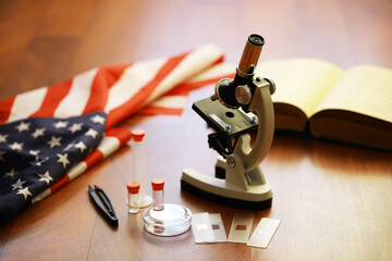 Microscope and Scientific Tools with American Flag and Open Book on Wooden Surface