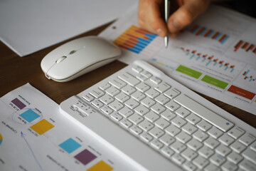 Hand Analyzing Business Financial Charts on Modern White Keyboard and Mouse Workstation
