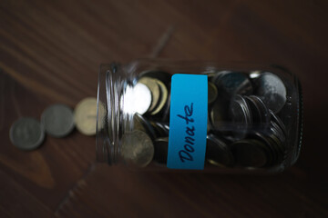 Donation Jar Filled with Coins on Wooden Surface - Fundraising, Savings, Charity Concept © alexkich