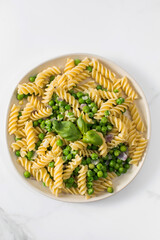 Vegetarian pasta with boiled green peas and basil on plate