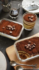 Gluten free tiramisu with homemade sponge cake and eggless cream, topped with dark chocolate and cocoa powder, on a wooden board and black background. Selective focus