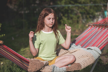 cute red-haired teenage girl sitting on a hammock in the lotus position