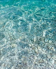 Some fish swim in the cristalline sea in Elba island. Abstract sun ripple patterns in clear wavy shallow sea water background
