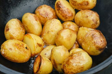 Whole potatoes in boiling oil on frying pan. Preparing food outdoors.  Shallow depth of field