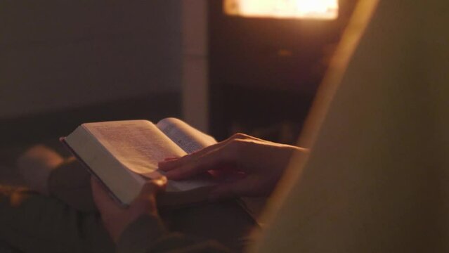 A woman sitting on the floor next to the sofa and reading a book by the fireplace. Atmosphere of comfort and warmth in the house.