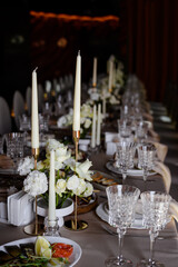 White candles in candelabra and white roses in glass vase on the wedding table decoration. 