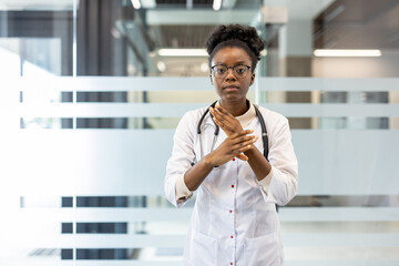 Confident doctor in a white coat with stethoscope making a hand gesture in a modern medical office setting.