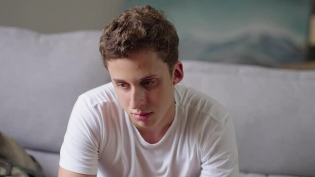 Sad teenage boy sit on sofa at home, lost in thoughts, looks into distance, think, looks upset experiences first unrequited love, having problems in school feel insecure. Teen problem concept
