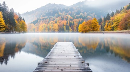 Misty autumn lake surrounded by vibrant, colorful trees. A wooden pier extends into the calm water, reflecting the serene, tranquil beauty of the fall landscape.