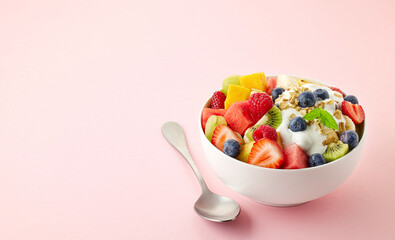 Bowl of fresh fruit salad, muesli and greek yogurt on light pink background