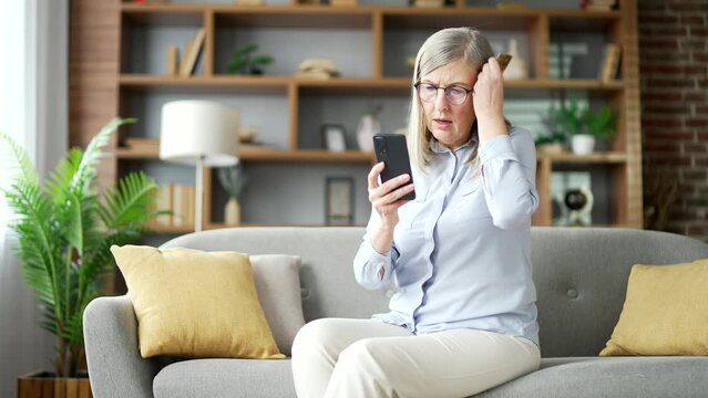 Frustrated senior female discovered fraud while entering credit card number on phone sitting at home. Upset elderly woman saw that money was stolen from her account. She became a victim of deception