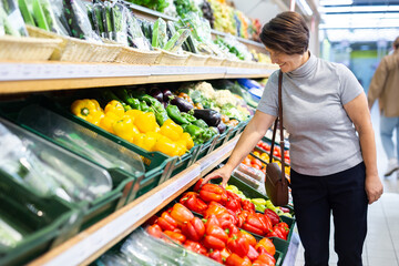 Elderly woman chooses pepper in vegetable and fruit department