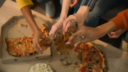 Unrecognizable group of people friends diversity buddies together gathering party drinking beer eating popcorn delivery pizza watching clink glass bottles clinking men women girls guys friendship home