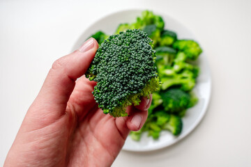 Broccoli in a woman's hand against the background of a plate of broccoli. Broccoli on a white plate.