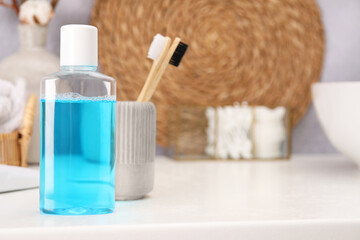 Bottle of mouthwash and toothbrushes on white table in bathroom, space for text