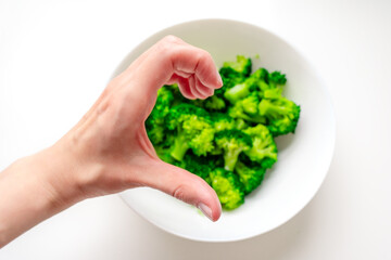 A woman's hand depicts half a heart over a plate of broccoli. Love for broccoli. Broccoli on a white plate.