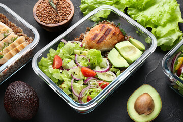 Healthy meal. Fresh salad, avocado, cutlet and buckwheat in glass container near other products on black table