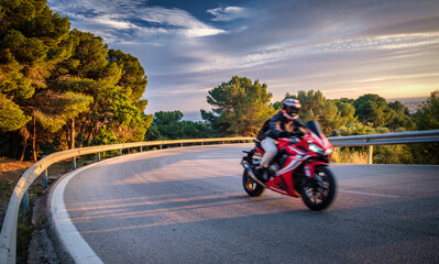 Daring motorcyclist takes sharp turn on scenic, sunlight-bathed route, fully equipped in safety gear with speed conveyed by motion blur.