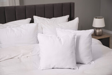 Many soft white pillows and duvet on bed indoors