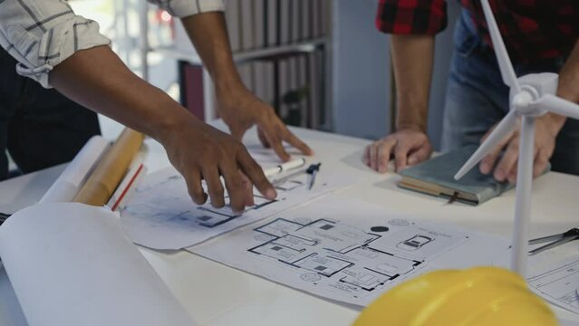 Engineers collaborate on a project, examining blueprints, and brainstorming ideas with architectural tools, sketch papers, and a scale model wind turbine