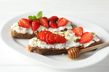 Delicious ricotta bruschettas with strawberry and pistachios served with honey on white table, closeup