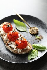 Delicious ricotta bruschetta with sun dried tomatoes, sauce, basil and milled pepper on grey table, closeup
