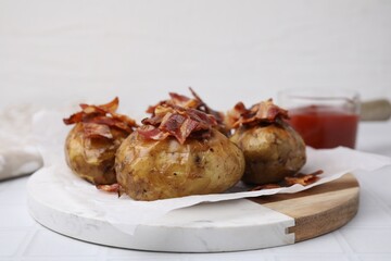 Delicious baked potatoes with bacon on white tiled table, closeup