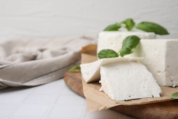 Fresh ricotta (cream cheese) and basil on white tiled table, closeup. Space for text