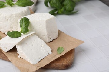 Fresh ricotta (cream cheese) and basil on white tiled table, closeup. Space for text