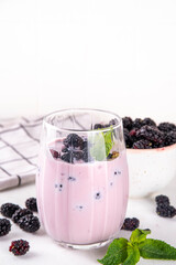 Mulberry shake, smoothie or yogurt drink on portioned glass, with a lot of fresh organic mulberry berries and mint, on white kitchen table, copy space