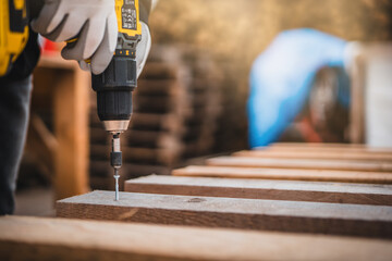 Close up man hand holding electric cordless screwdriver machine and screws lie for screwing a screw assembling wood construction. Iron screw, screws as a background, wood screw, concept industry.