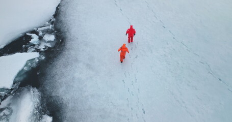 Two man in immersion suits walk Antarctica ocean ice. People explore South Pole. Group of scientists in orange wetsuits research climate and arctic wild nature. Aerial top trekking drone shot © mozgova