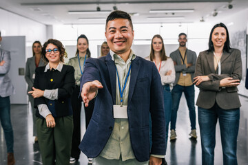 Obraz premium Portrait of young Asian CEO standing in front of his colleagues with his hand outstretched ready to shake hands.