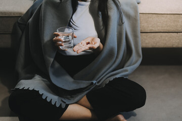 Cold medicine and sick woman drinking hot beverage to get well from flu, fever and virus. Dirty paper towels and tissues on table. Ill person wearing warm woolen stocking socks in winter.
