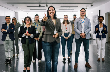 Obraz premium Portrait of young female CEO standing in front of her multiracial colleagues and gives thumbs up.