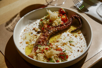 Grilled octopus on bed of pearled couscous and olive oil nicely served on the restaurant table