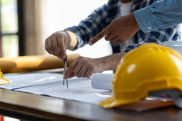 Brainstorming group of architects and engineers discuss building blueprint design on laptop and construction project planning on wooden table in office.