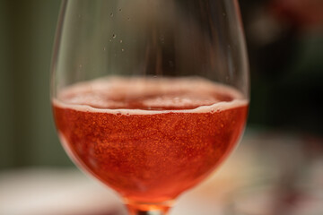 vista macro di un calice, messo su un tavolo apparecchiato, riempito per metà da una bevanda dolce, gassata e frizzante di colore rosso