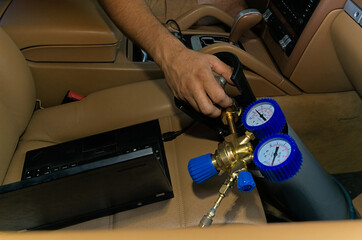 A small portable nitrous oxide cylinder with gauges and a valve, placed in a car's interior with a computer on the seat.