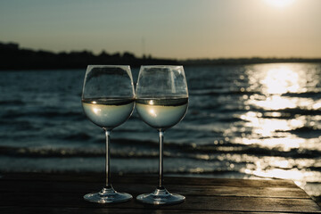Two glasses of wine on wooden table near river at sunset. Space for text