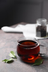 Tasty hot tea in cup and leaves on grey table, closeup