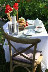 Beautiful bouquet of tulips and freshly baked waffles on table served for tea drinking in garden