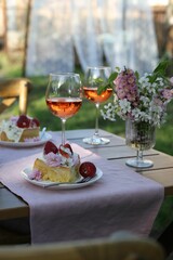 Vase with spring flowers, wine and cake on table served for romantic date in garden