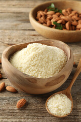 Fresh almond flour in bowl, spoon and nuts on wooden table, closeup