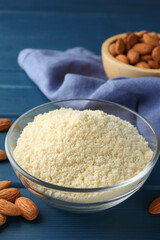 Fresh almond flour in bowl and nuts on blue wooden table, closeup