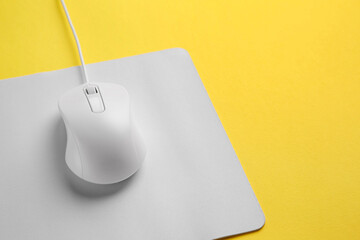 Wired mouse with mousepad on yellow background, closeup. Space for text