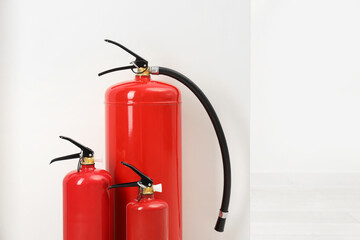 Fire extinguishers near light wall indoors, space for text