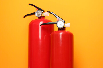Two fire extinguishers on orange background, closeup