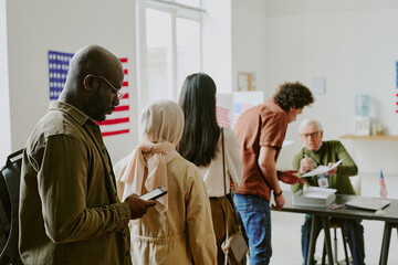 Young African American male citizen holding smartphone standing in line at voting station on...
