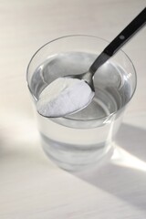 Glass of water and spoon with baking soda on light background